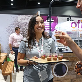 IFT FIRST exhibitor smiles while handing out sample cups to attendees